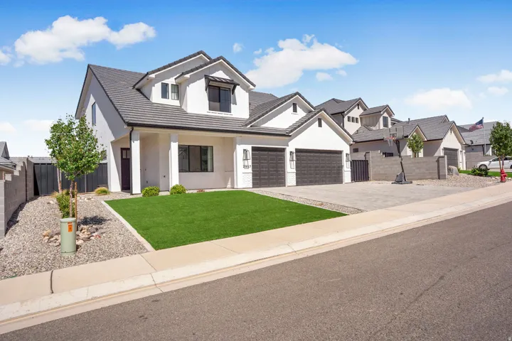 White stucco exterior with dark gray roof, two-car garage, and a paver driveway