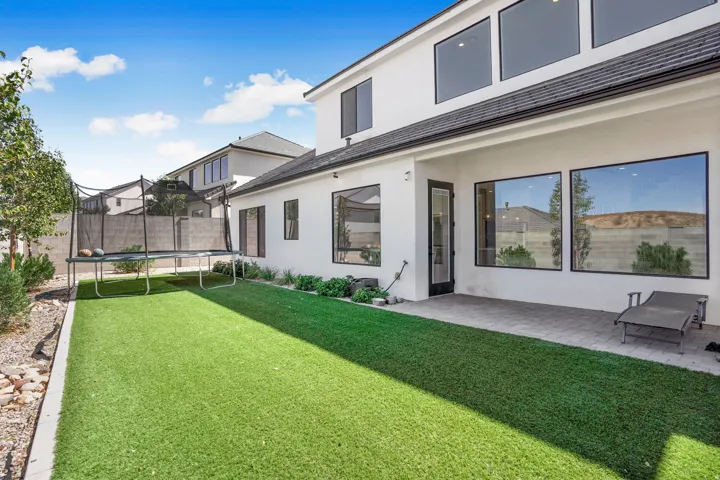 Expansive rear exterior featuring a white stucco facade, black-framed windows, artificial turf, and a paver patio