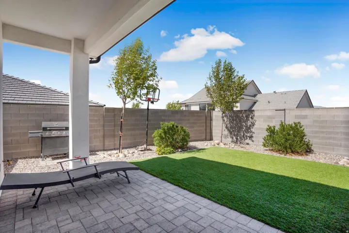Covered patio with paver flooring, artificial turf, and block wall fencing