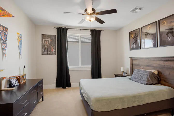 Carpeted flooring, window with dark drapes, ceiling fan with light fixture, and a dark wood-finish headboard