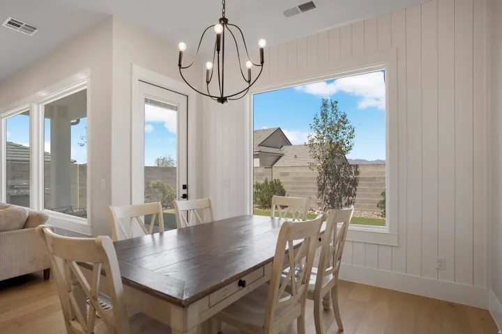 Spacious interior with wood-finish flooring, a contemporary chandelier, large windows, and vertical paneling