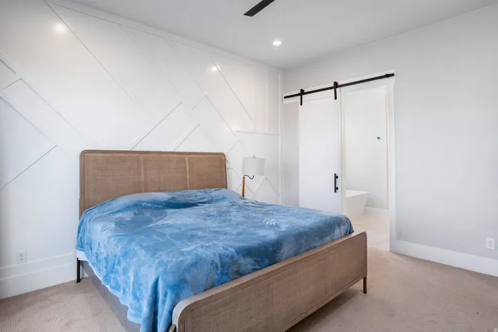 Accent wall with geometric paneling, recessed lighting, ceiling fan, carpeted flooring, and a sliding barn door leading to an en-suite bathroom