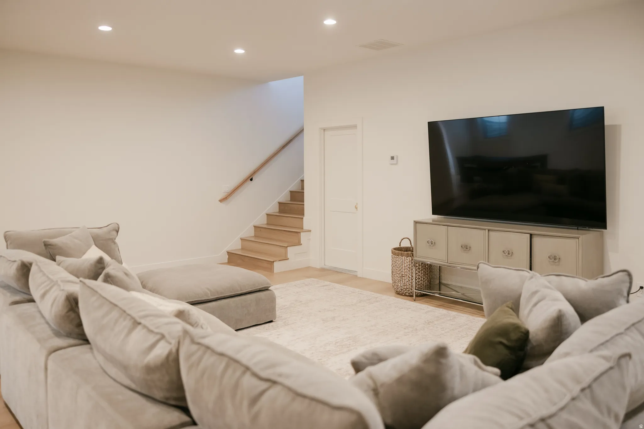 Recessed ceiling lighting, light wood-finish flooring, and a light wood handrail with matching stairs