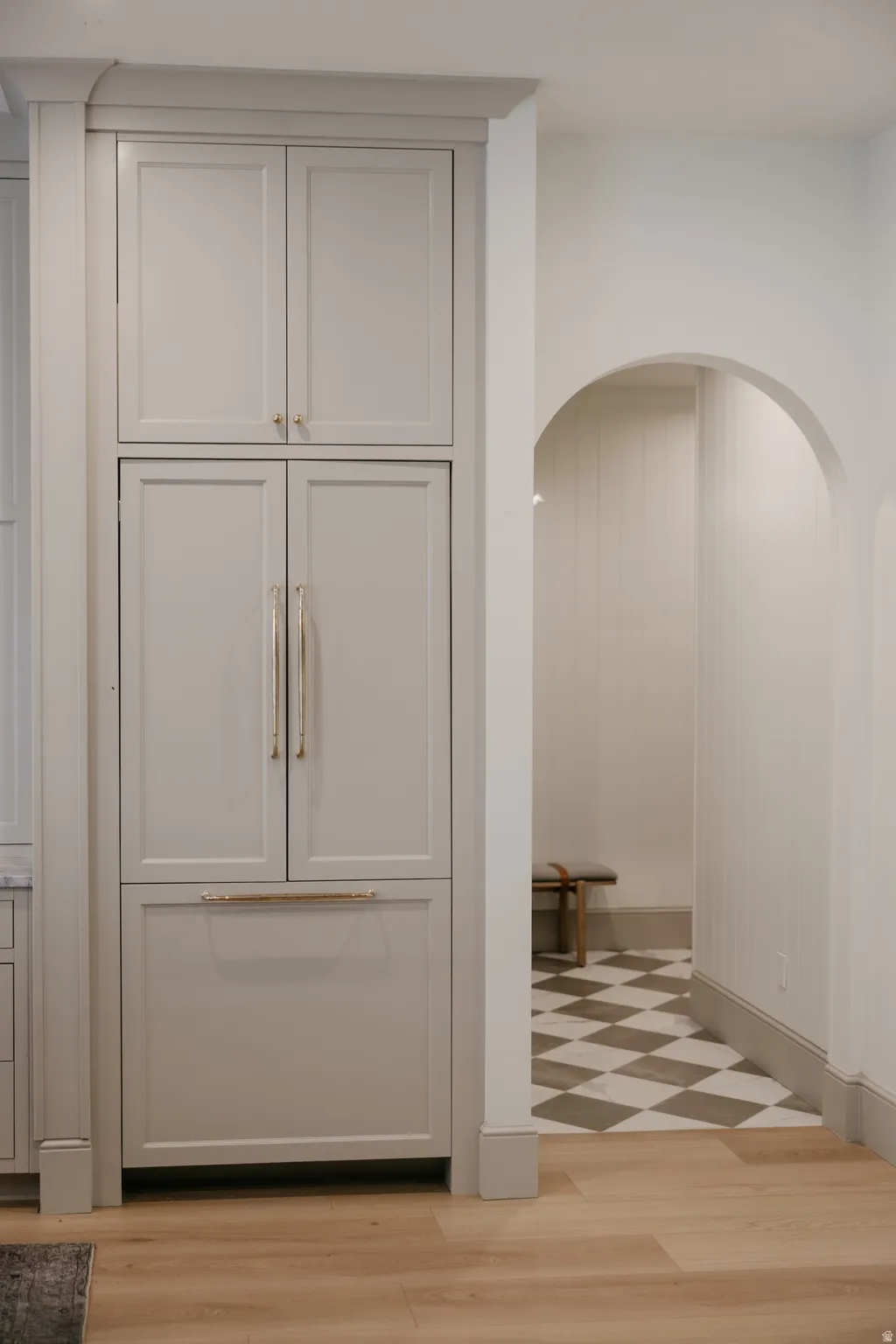Integrated panel-ready refrigerator with custom cabinetry, light wood-finish flooring, and arched entryway with checkerboard floor