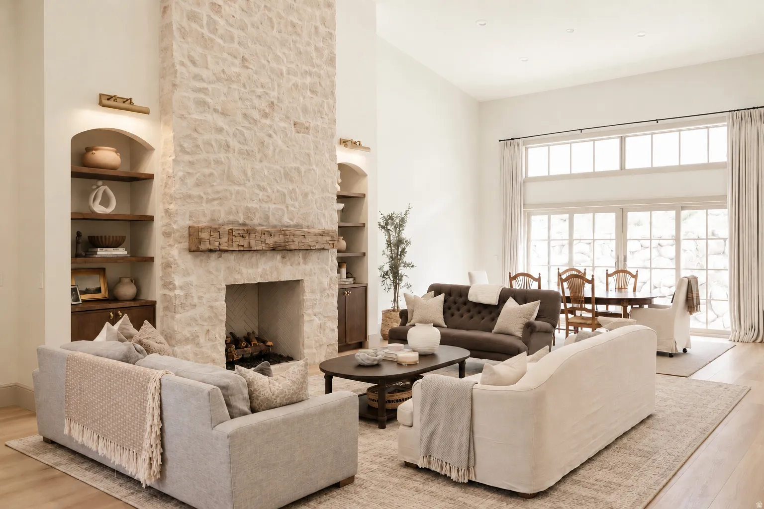 Stone-clad fireplace with a wood mantel, built-in shelving with integrated lighting, wood-finish flooring, and expansive glass doors with transom windows