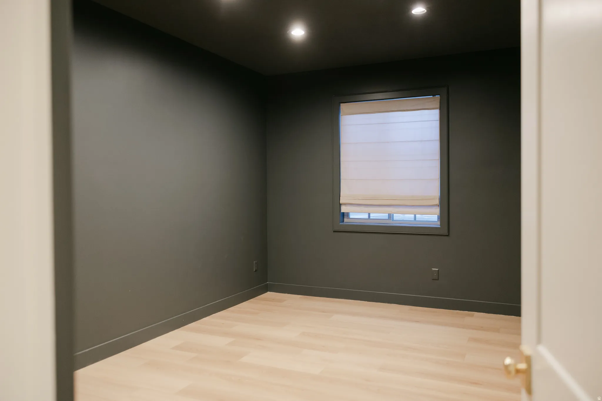 Recessed lighting, wood-finish flooring, and a single window with a Roman shade