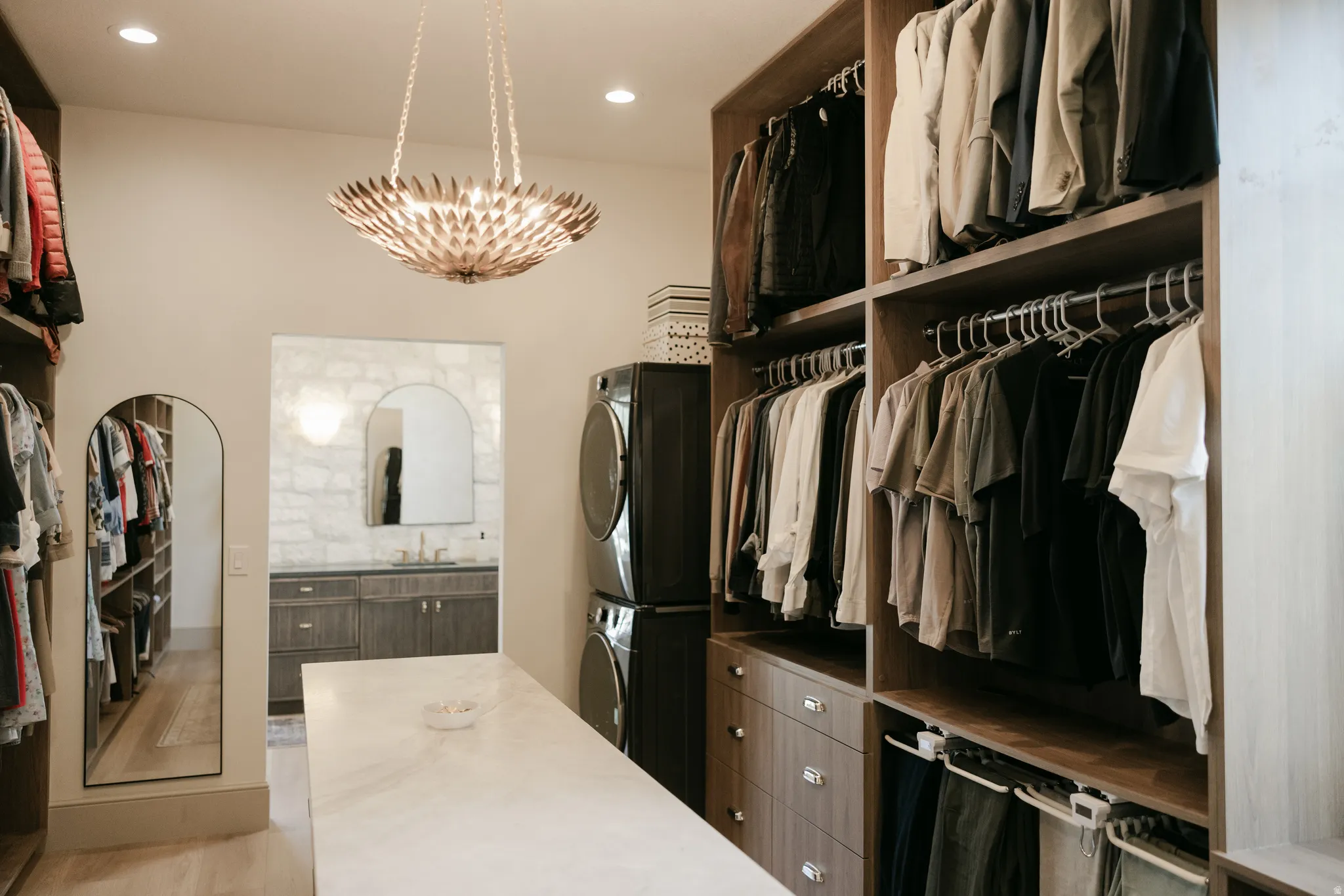 Custom built-in closet system with varied storage, central island with a stone-finish countertop, recessed lighting, and a decorative chandelier