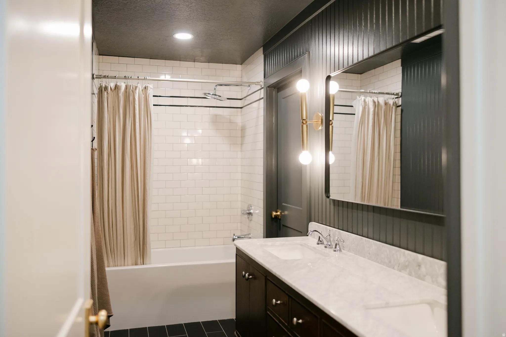 White subway tile shower surround with black accent lines, dark wood-finish dual vanity with undermount sinks, and wall-mounted vanity lighting