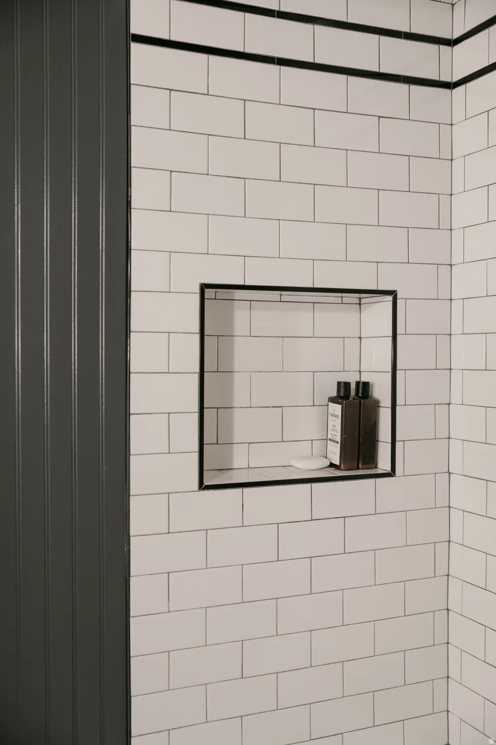 Subway tile walls with dark grout, a recessed shower niche, and dark accent trim