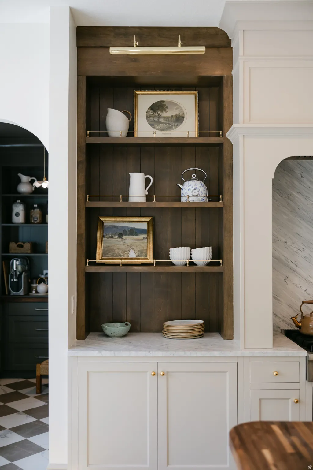 Built-in cabinetry with light-colored doors, a light-toned countertop, and a dark wood-finish open shelving unit with brass railings and integrated lighting