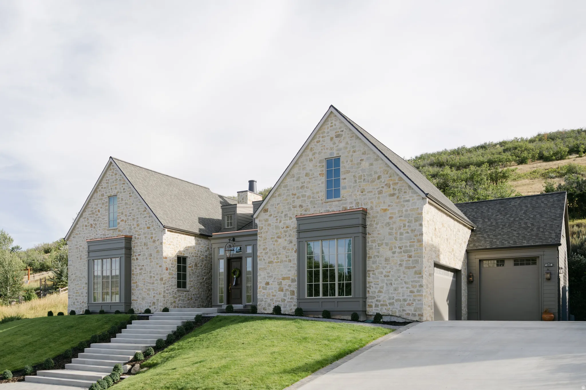 Stone facade residence featuring a multi-gable roofline, a prominent bay window, an attached two-car garage, and a concrete driveway
