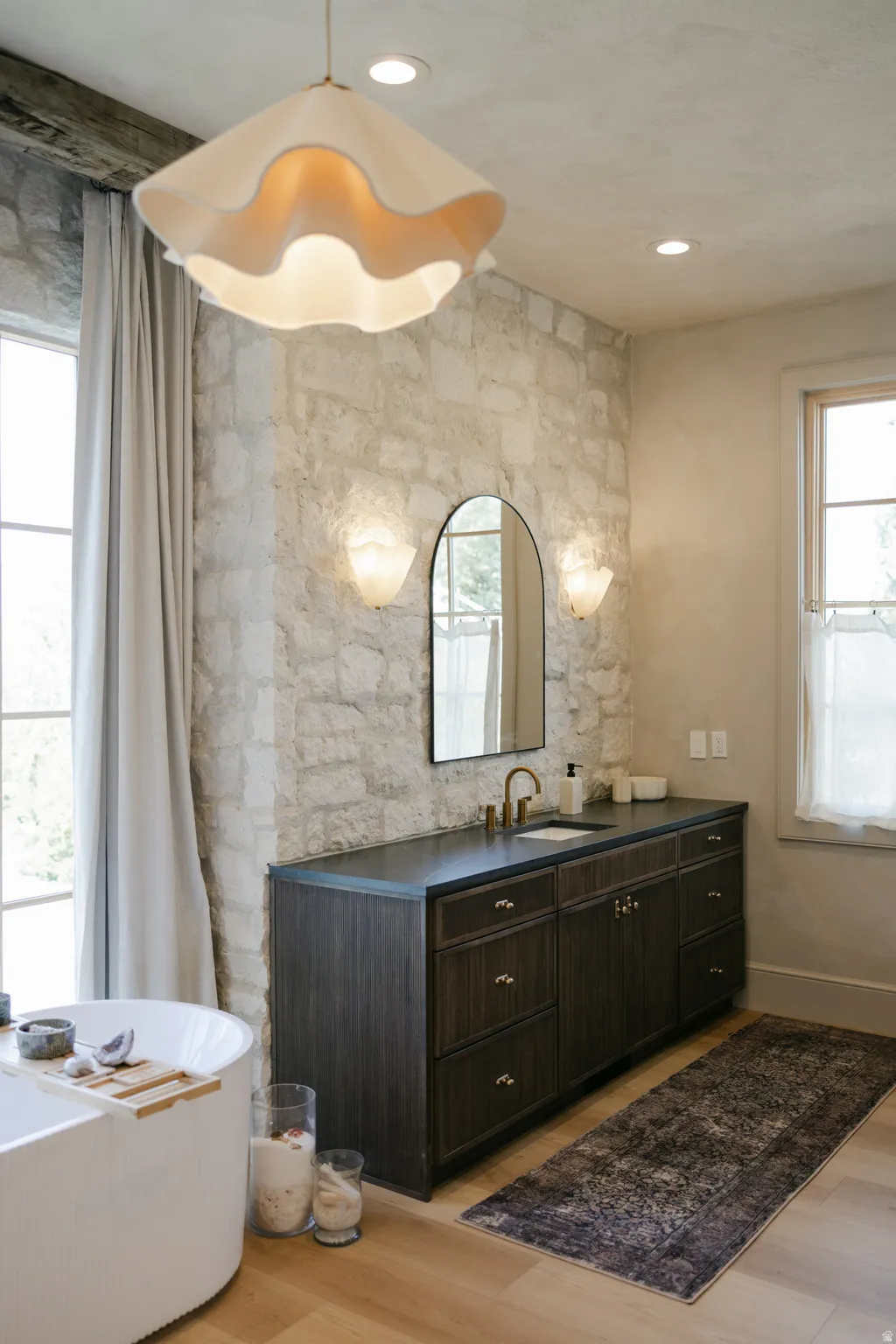 Stone accent wall with sconce lighting and an arched mirror