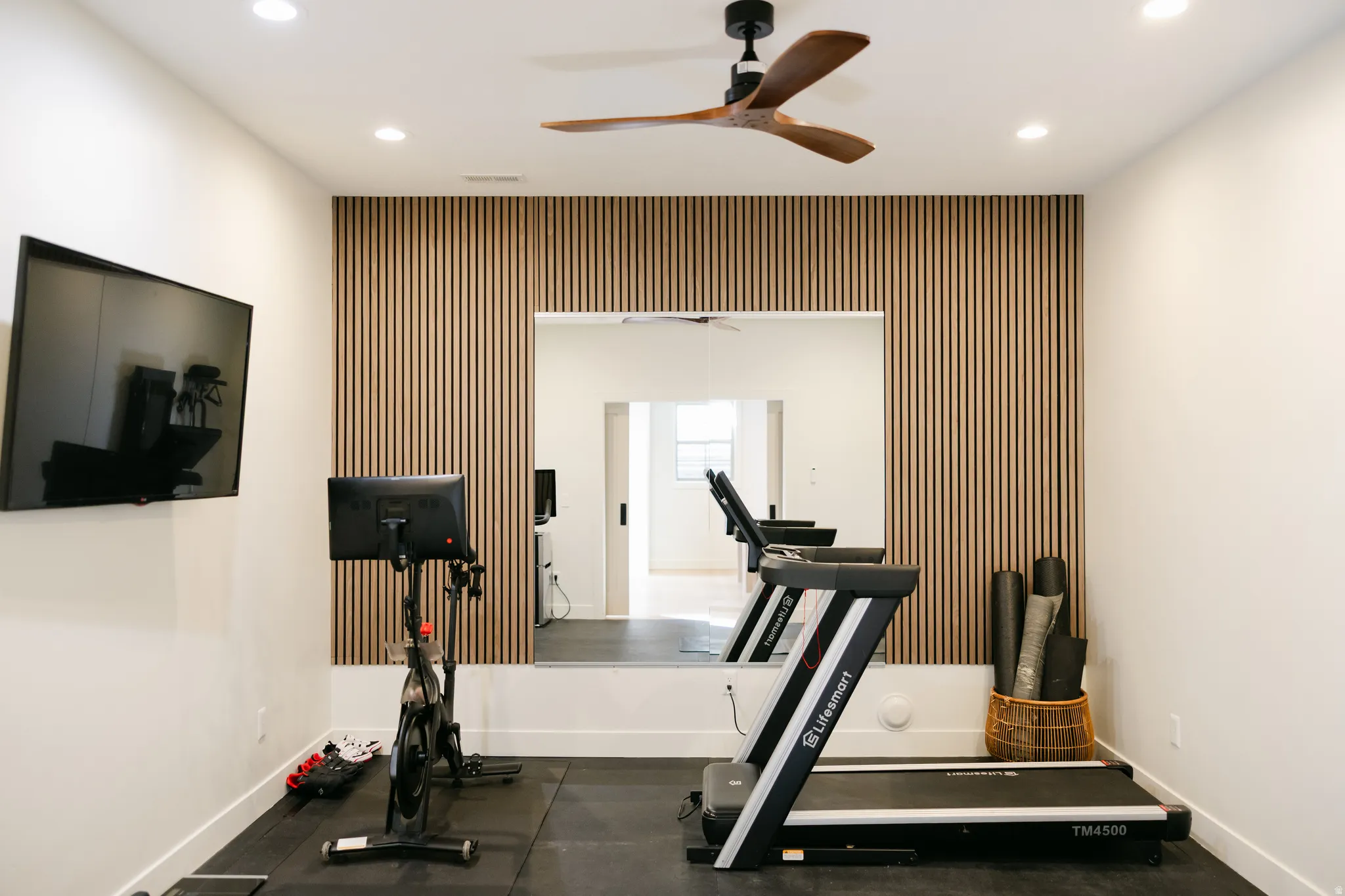 Recessed lighting, wood-slat accent wall, large wall-mounted mirror, ceiling fan with wood-finish blades, and white walls