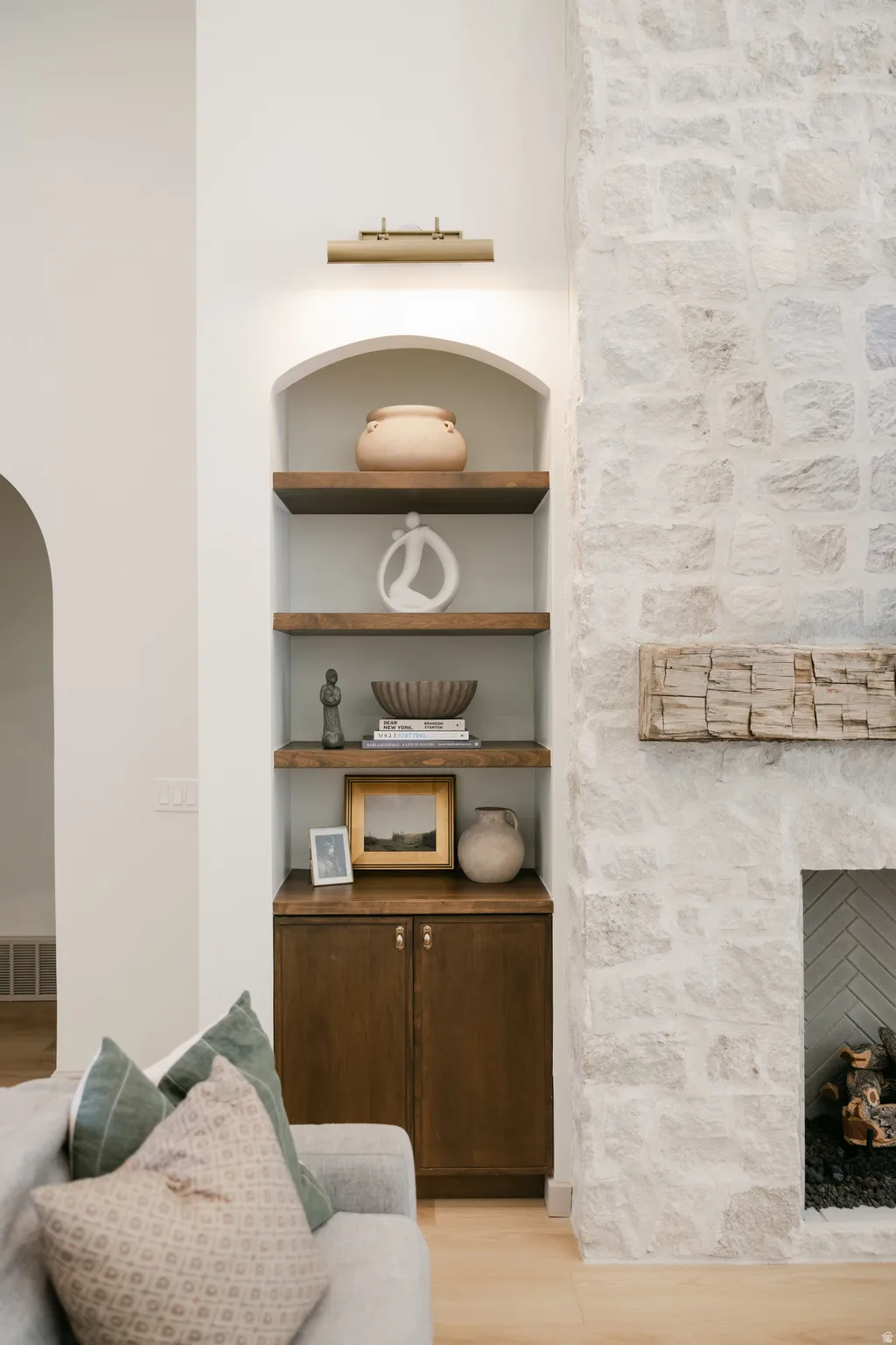 Arched built-in shelving with wood-finish shelves, warm wood-finish cabinetry, and an integrated picture light