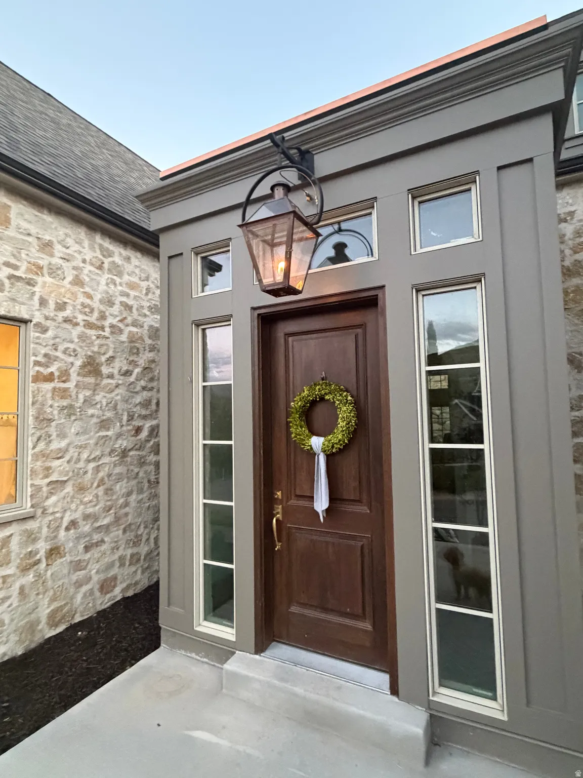 Stone veneer exterior with a wood-panel entry door, flanked by sidelight windows and transom windows