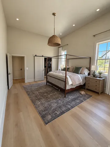 Vaulted ceiling with recessed lighting and a central pendant fixture, light wood-finish flooring, and white barn doors