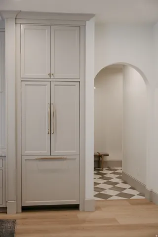 Integrated panel-ready refrigerator with custom cabinetry, light wood-finish flooring, and arched entryway with checkerboard floor