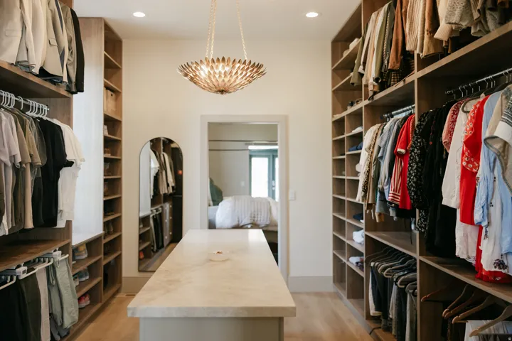 Spacious custom closet featuring wood-finish shelving, built-in clothing racks, a central island with a light-toned countertop, and recessed lighting