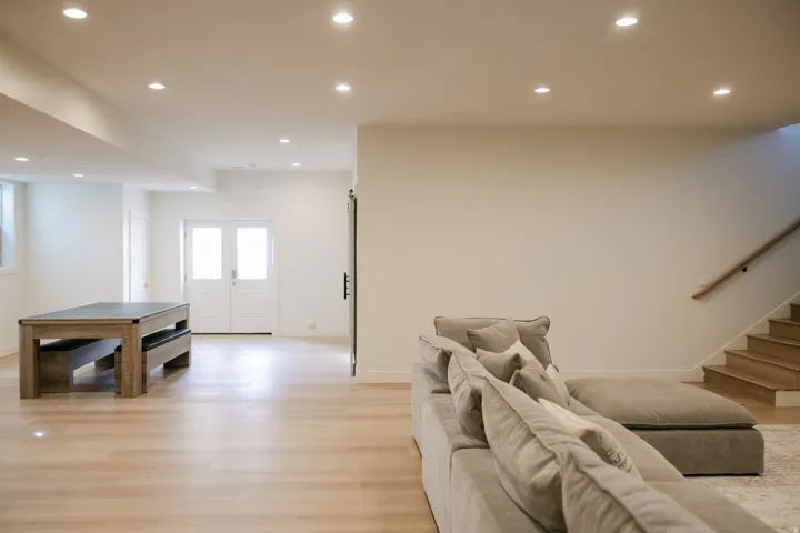 Recessed lighting illuminating light wood-finish flooring and a staircase with a wooden handrail