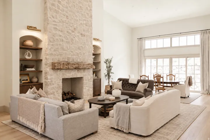 Stone-clad fireplace with a wood mantel, built-in shelving with integrated lighting, wood-finish flooring, and expansive glass doors with transom windows