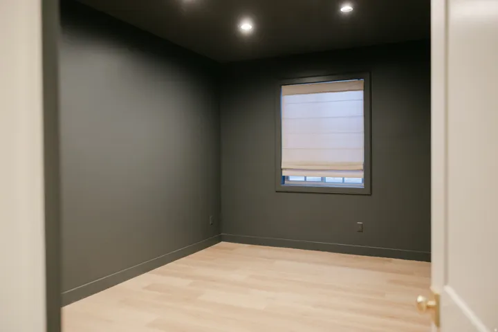 Recessed lighting, wood-finish flooring, and a single window with a Roman shade
