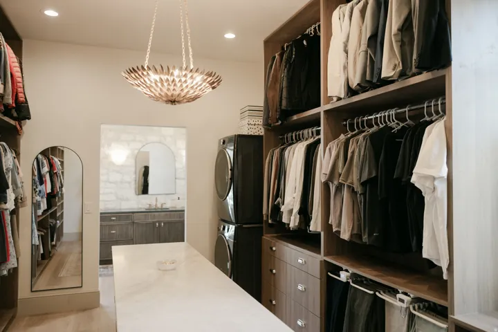 Custom built-in closet system with varied storage, central island with a stone-finish countertop, recessed lighting, and a decorative chandelier