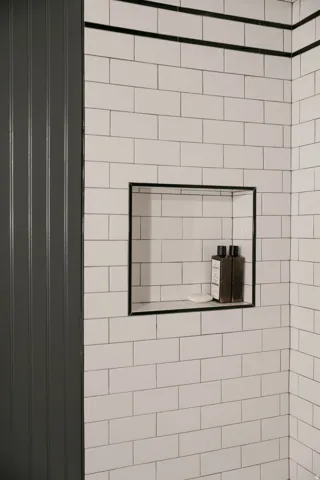 Subway tile walls with dark grout, a recessed shower niche, and dark accent trim