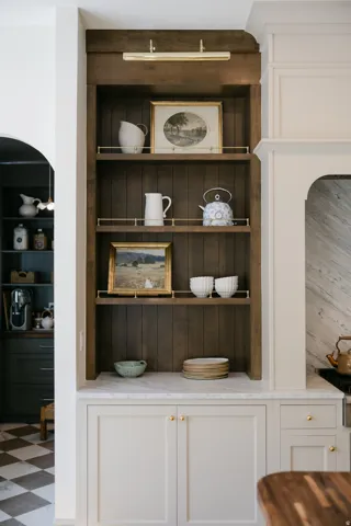Built-in cabinetry with light-colored doors, a light-toned countertop, and a dark wood-finish open shelving unit with brass railings and integrated lighting