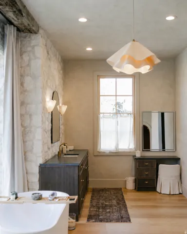 Freestanding bathtub, wood-finish flooring, stone accent wall, recessed lighting, and a dark wood-finish vanity with a gold-tone faucet