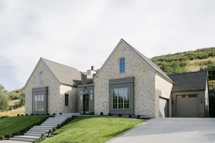 Stone facade residence featuring a multi-gable roofline, a prominent bay window, an attached two-car garage, and a concrete driveway