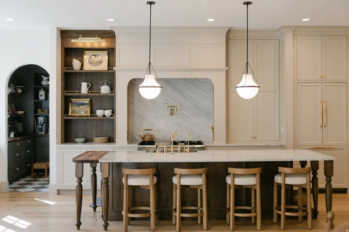 Expansive kitchen island with a light-toned countertop, built-in gas range, integrated hood vent, full-height cabinetry, and wood-finish flooring