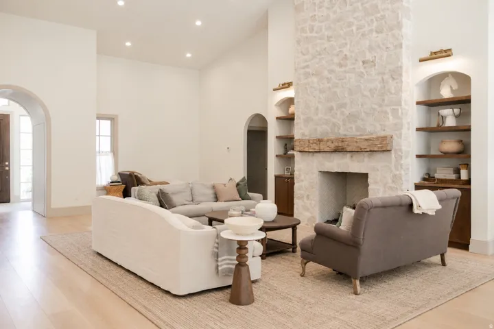 Vaulted ceilings, wood-finish flooring, stone-clad fireplace with wood mantel, recessed lighting, and arched doorways