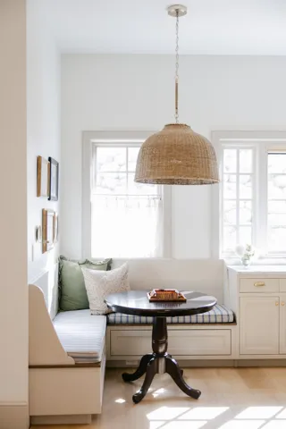 Built-in banquette seating with integrated storage, wood-finish flooring, multiple windows, and a woven pendant light fixture