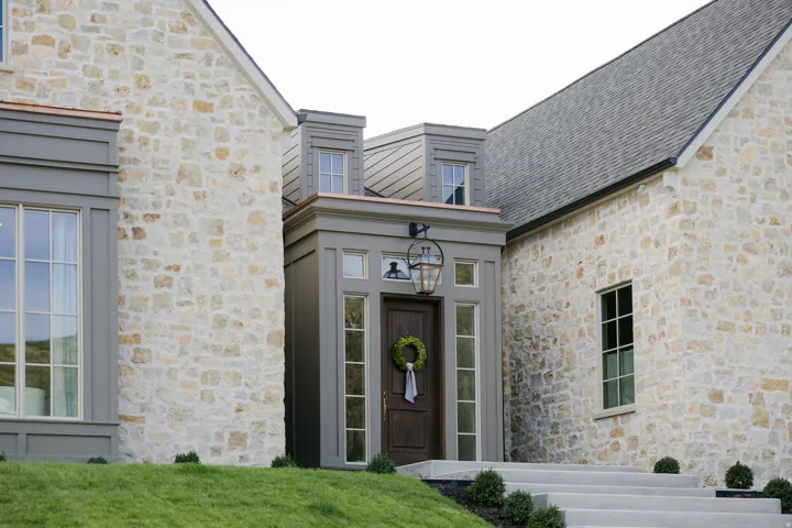 Stone veneer exterior with gray trim, dark wood entry door, and dormer windows