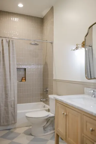 Bathroom featuring a built-in tub with tile surround, a recessed shower niche, a wood-finish vanity with a stone countertop, and checkerboard floor tiles