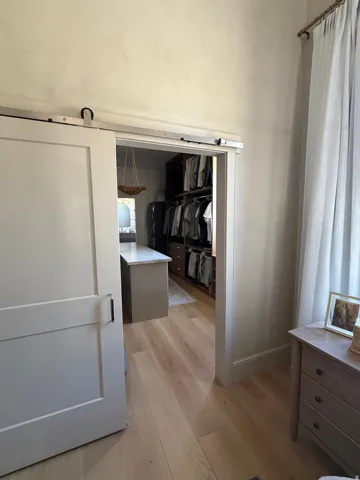 Barn door entry to a closet featuring wood-finish flooring and built-in shelving