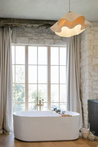 Freestanding ribbed soaking tub with a floor-mounted brass fixture, set against a large grid-pattern window