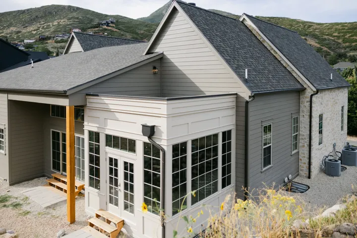 Exterior featuring gray siding, stone accent walls, multiple windows, and a sunroom with French doors