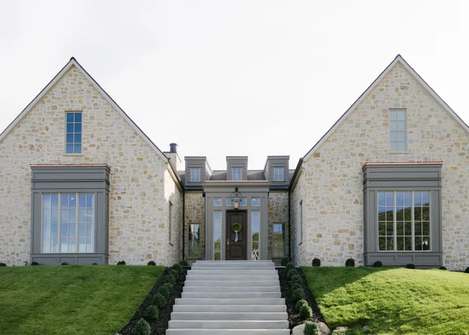 Stone facade with gabled rooflines, symmetrical bay windows, and a central entryway with transom windows