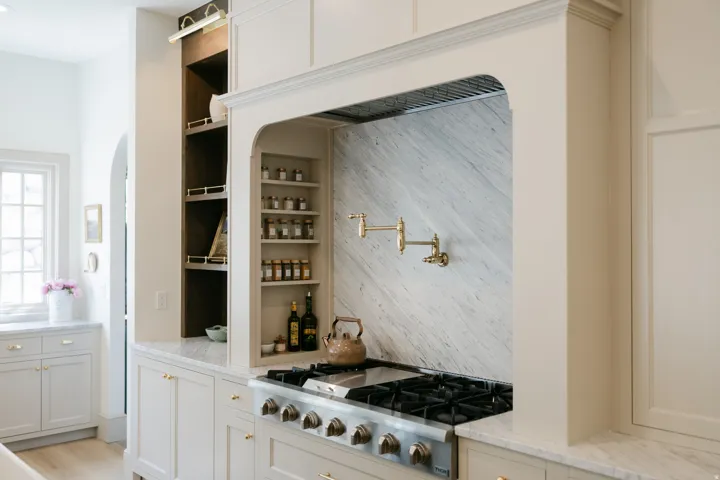 Professional-grade range with a brass pot filler, custom range hood, and integrated spice shelving