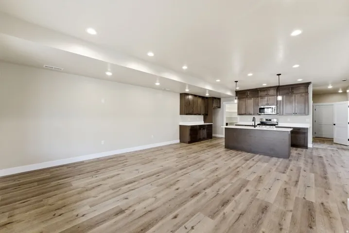 Wood-finish flooring throughout, recessed lighting, dark wood-finish cabinetry, light-toned countertops, and a kitchen island with a built-in sink