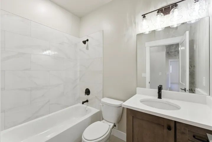 Bathroom featuring a built-in bathtub with subway tile surround, dark wood-finish vanity with an integrated sink, and an overhead vanity light fixture