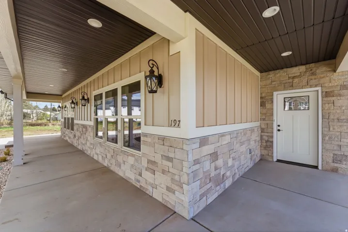 Stone veneer and vertical siding exterior with a covered concrete porch, decorative outdoor lighting, and an entry door featuring an etched glass pane