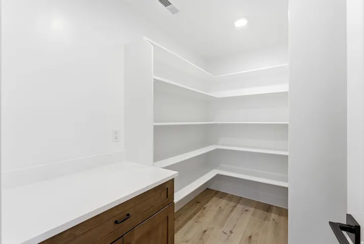 Expansive walk-in pantry with wrap-around shelving, wood-finish flooring, recessed lighting, and a built-in cabinet with a solid surface countertop