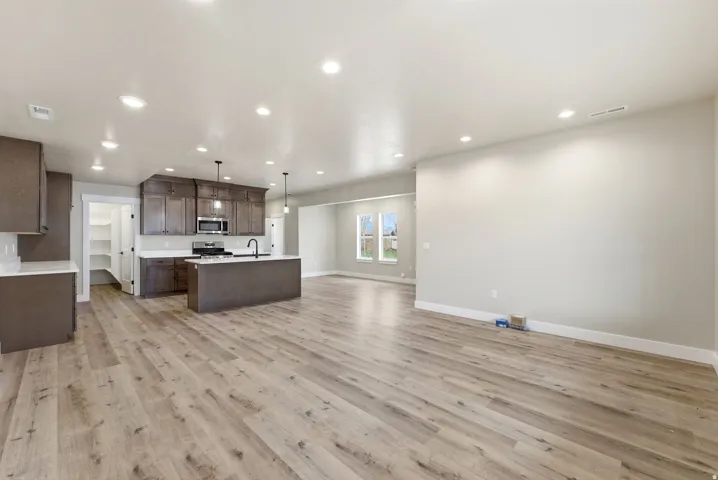 Spacious interior featuring wood-finish flooring, recessed lighting, and a kitchen with dark wood cabinetry, white countertops, and stainless steel appliances