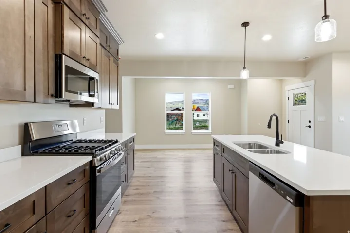 Kitchen featuring wood-finish cabinetry, stainless steel appliances, white countertops, and a center island with a double basin sink and a matte black faucet