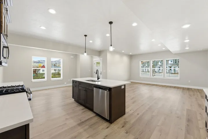 Open concept living area with wood-finish flooring, recessed lighting, and a kitchen island featuring a sink and stainless steel dishwasher
