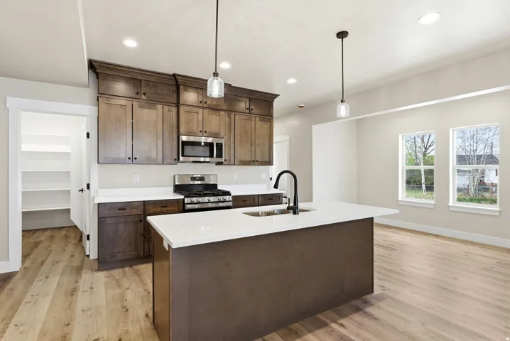 Kitchen featuring a center island with sink, stainless steel appliances, wood-finish flooring, recessed lighting, and a pantry with built-in shelving