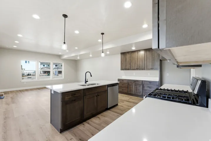 Open-concept kitchen featuring dark wood-finish cabinetry, a large kitchen island with a sink, stainless steel appliances, and light countertops