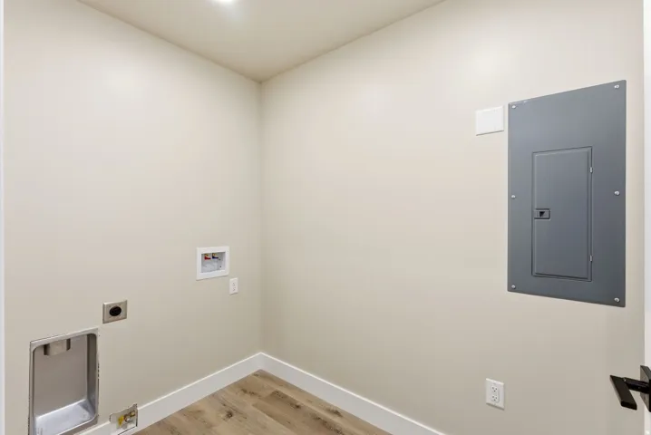 Recessed ceiling lighting, wood-finish flooring, white baseboards, wall-mounted electrical panel, and a black door handle